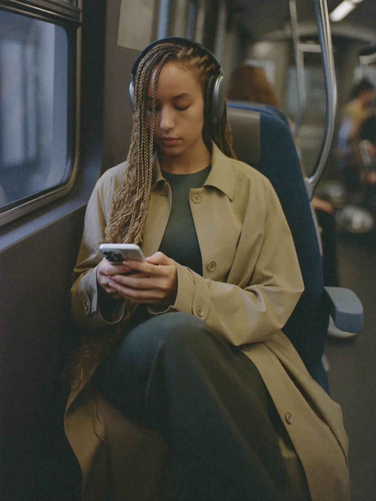 Mulher de tranças e fones de ouvido lê no celular sentada no metrô